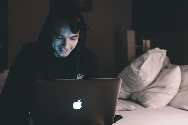 young adult using a macbook laptop in bed